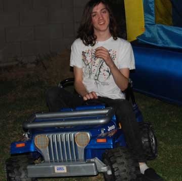 A person with long hair sitting in a blue toy Jeep outdoors
